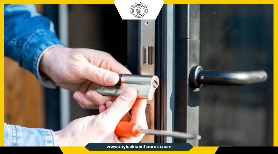 doorlockspins My Locksmith Aurora A locksmith holding a Euro profile cylinder lock next to an open door frame while holding a screwdriver.