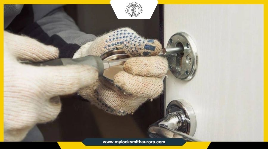 jammeddoorlockfixes My Locksmith Aurora A locksmith in work gloves using a screwdriver to repair a door lock mechanism.